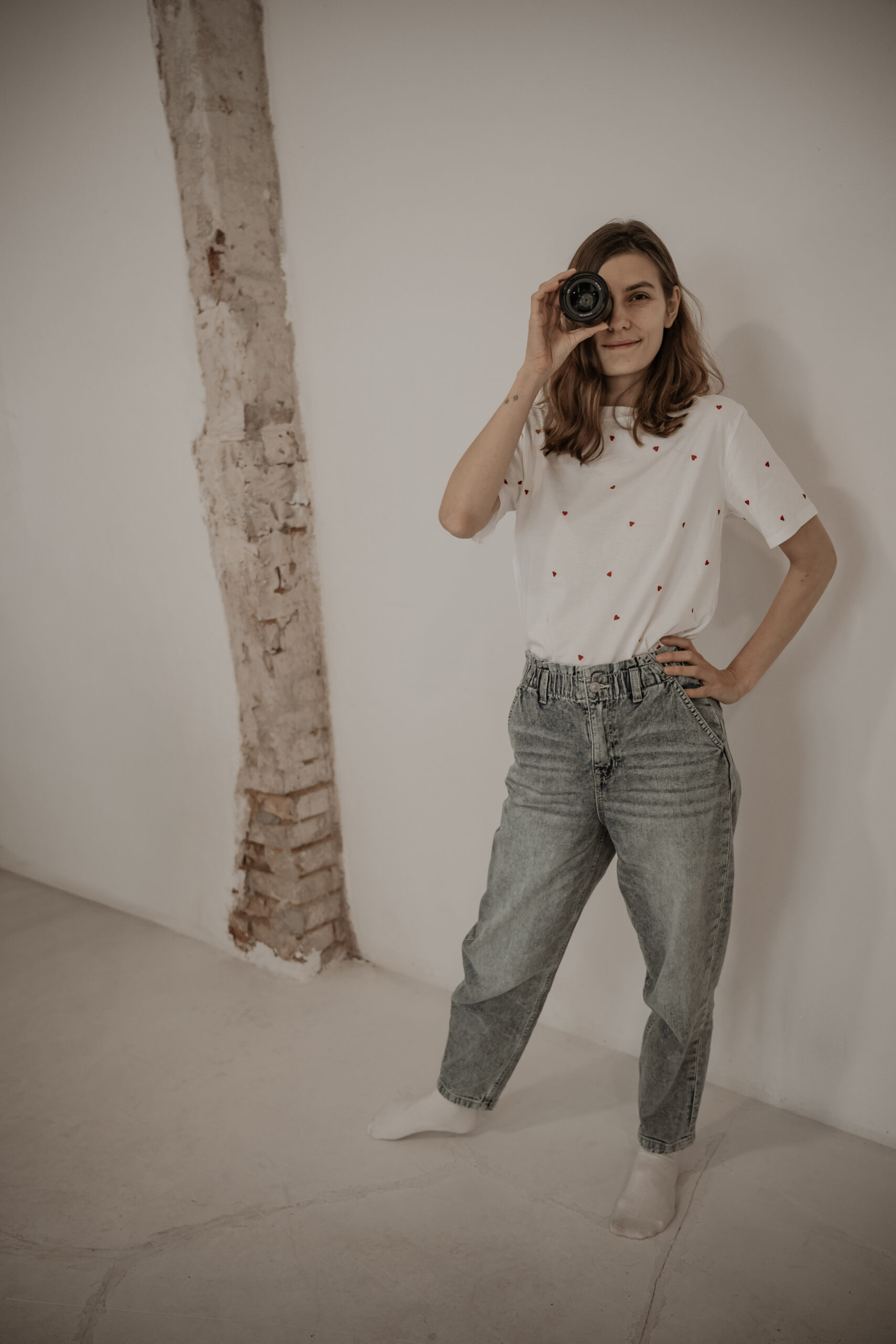 Fotografin hält sich ein Objektiv vor das rechte Auge und lächelt